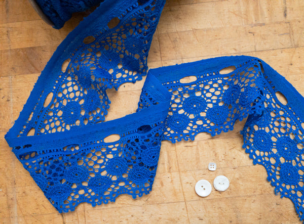 Royal blue macrame crochet trim on wood background and white buttons